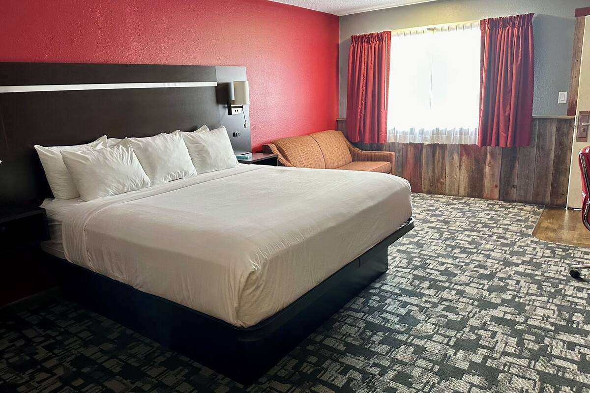A hotel room with a large bed, a nightstand, a chair, and a window with curtains.