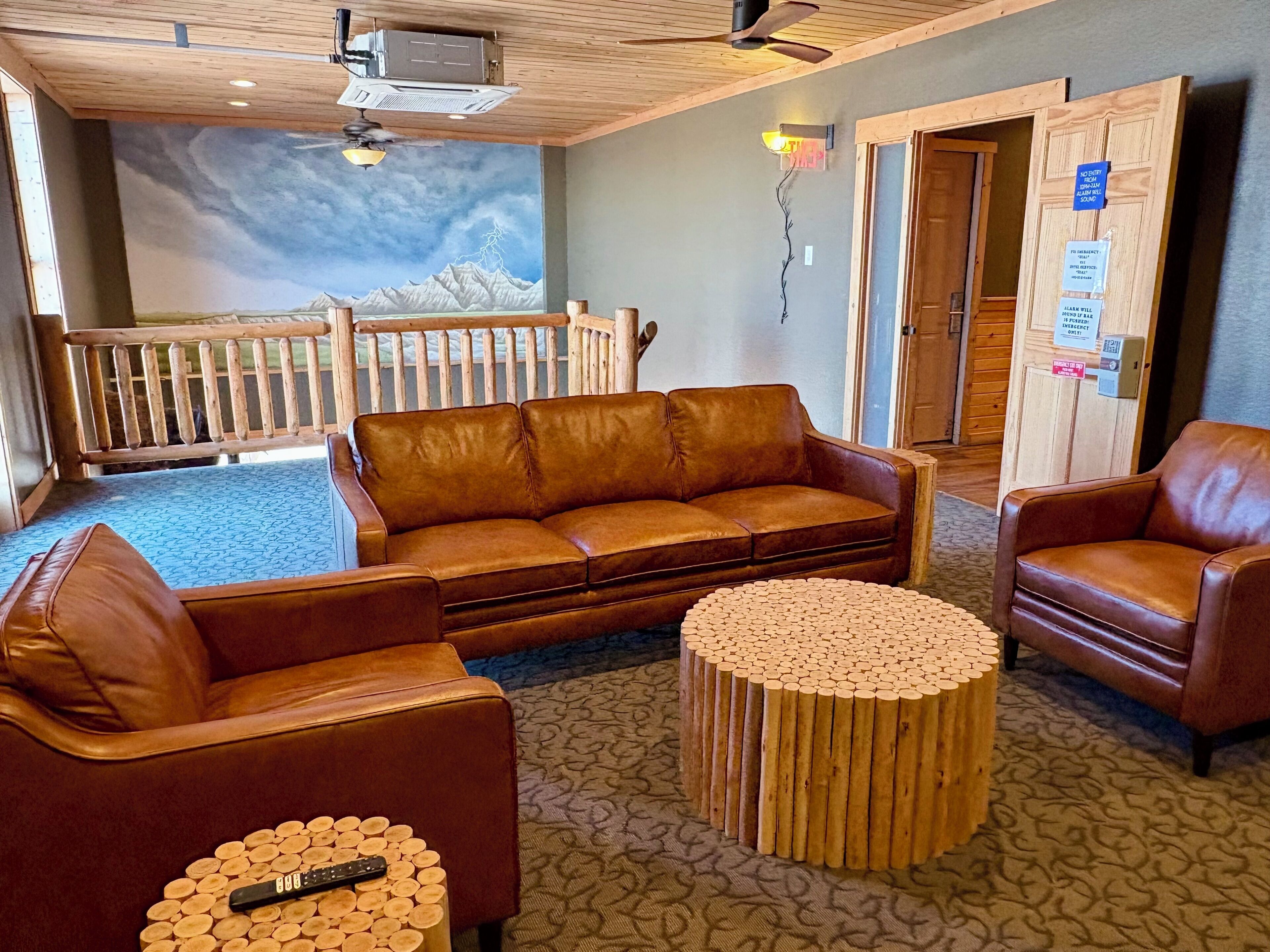 A cozy lounge area with a brown leather sofa, two wooden coffee tables, and a wooden bench.
