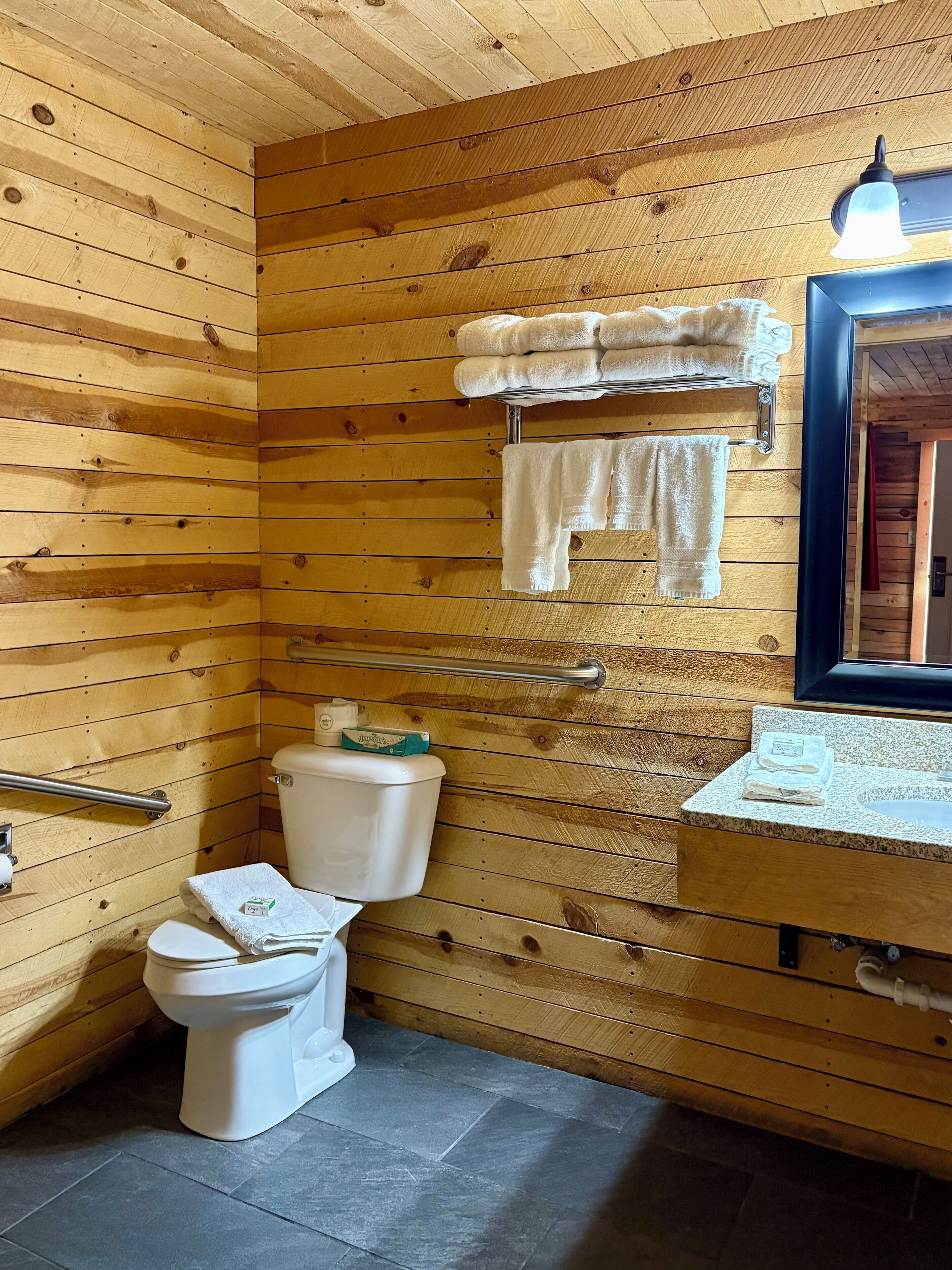 A wooden-paneled bathroom with a toilet, a sink, and a towel rack.