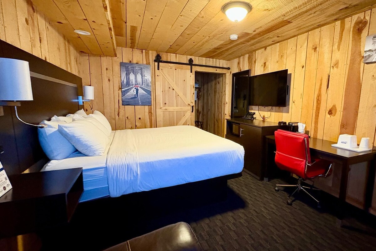 A hotel room with a bed, a desk, a chair, a television, and a door.