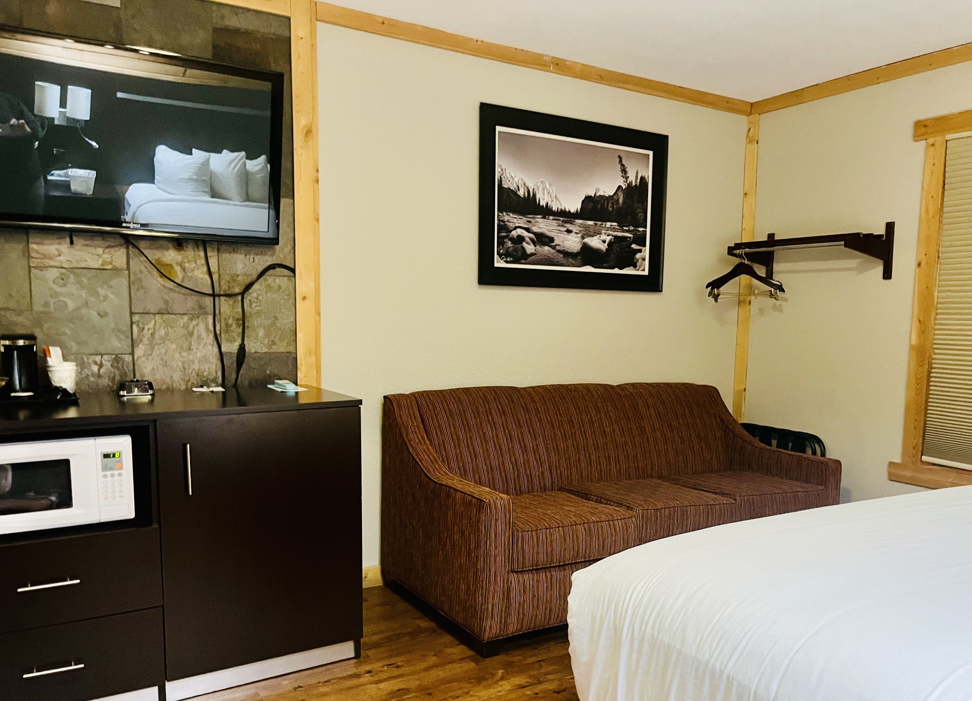 Une chambre d’hôtel avec un lit, un canapé marron, un téléviseur fixé à un mur en pierre, un tableau encadré et un meuble en bois contenant un four à micro-ondes.