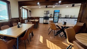 A dining area with wooden tables and chairs, a refrigerator, and a beverage dispenser. - Americas Best Value Inn Wall (Wall)