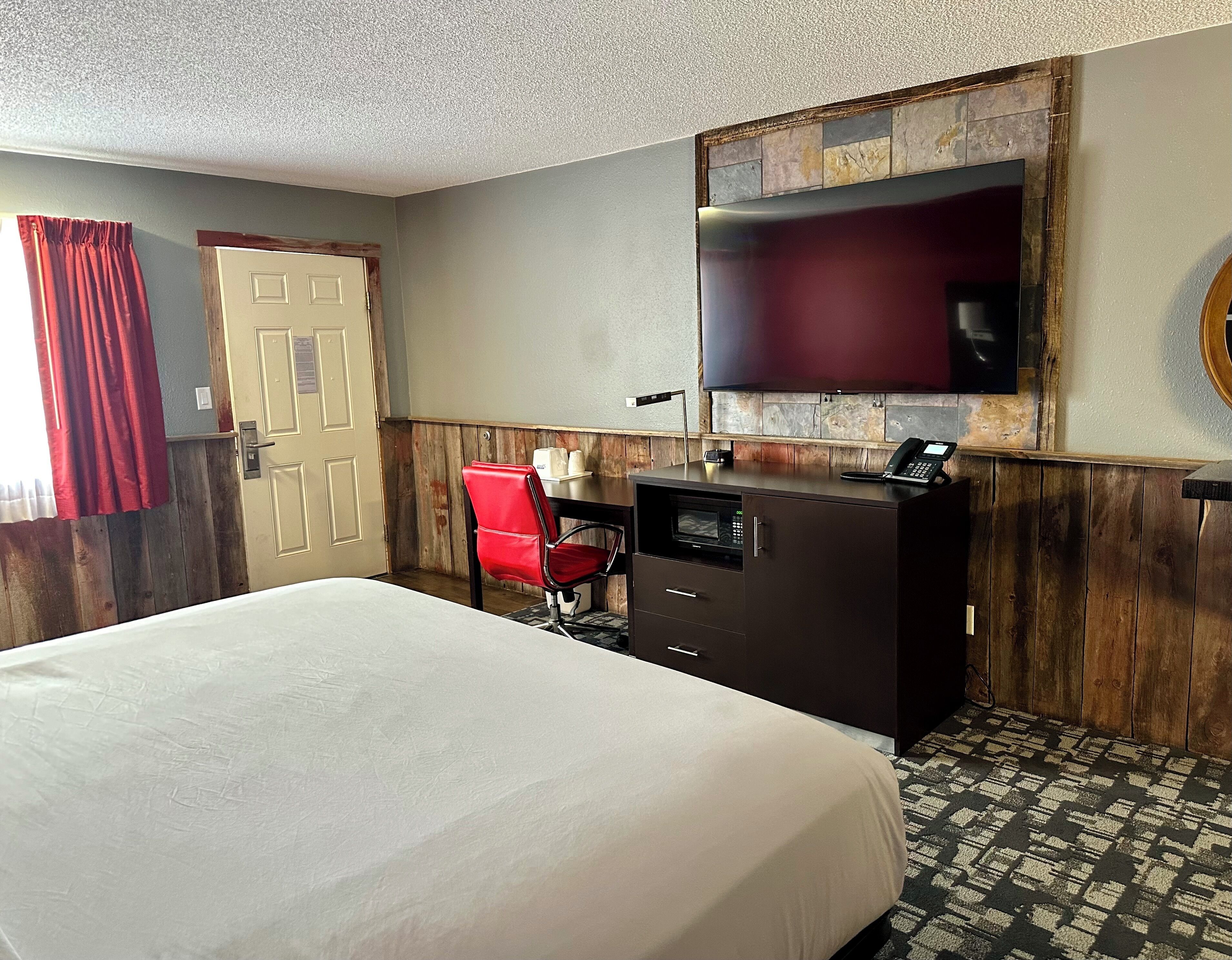 A hotel room with a bed, a desk with a chair, a telephone, and a television mounted on the wall.