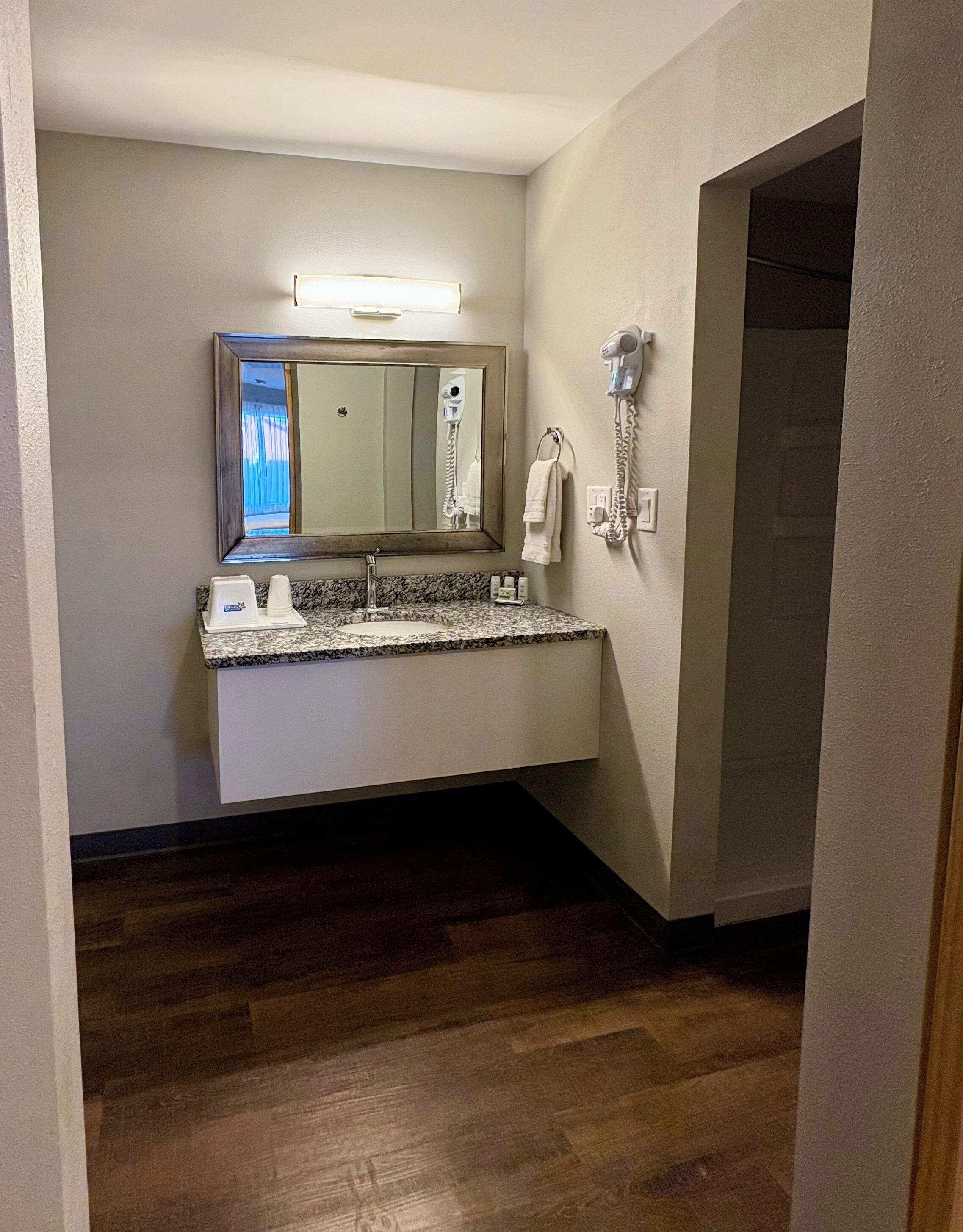 A bathroom with a granite countertop, a mirror, a hairdryer, and a towel rack.