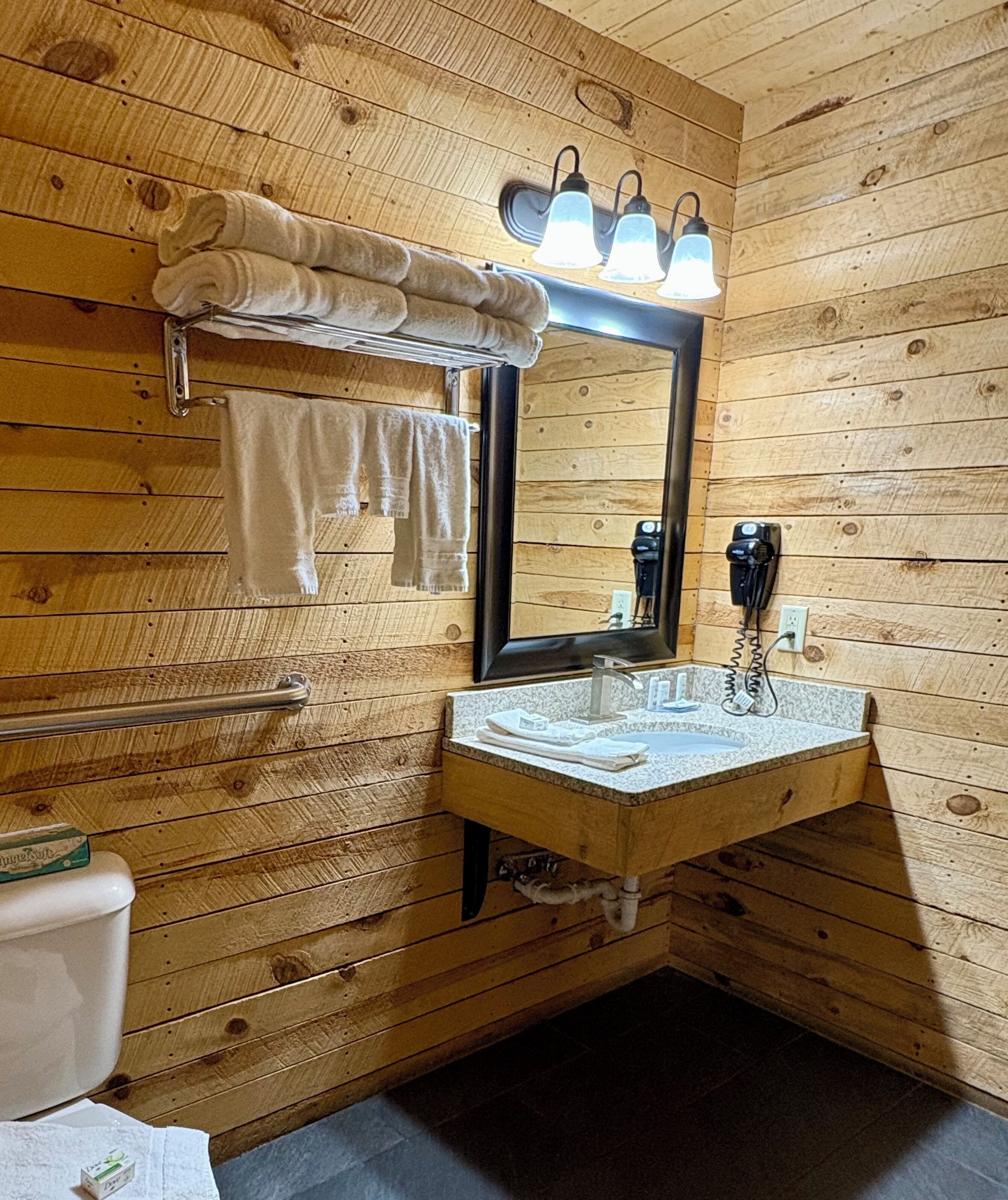 Casa de banho com painéis de madeira, uma pia, espelho, porta-toalhas e um secador de cabelo.