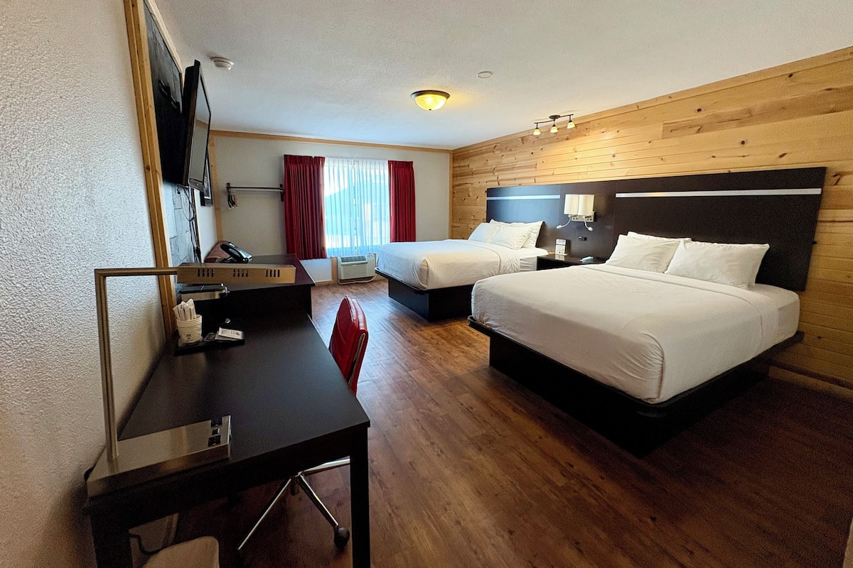 A hotel room with two beds, a desk, a chair, a TV, and a window with curtains.