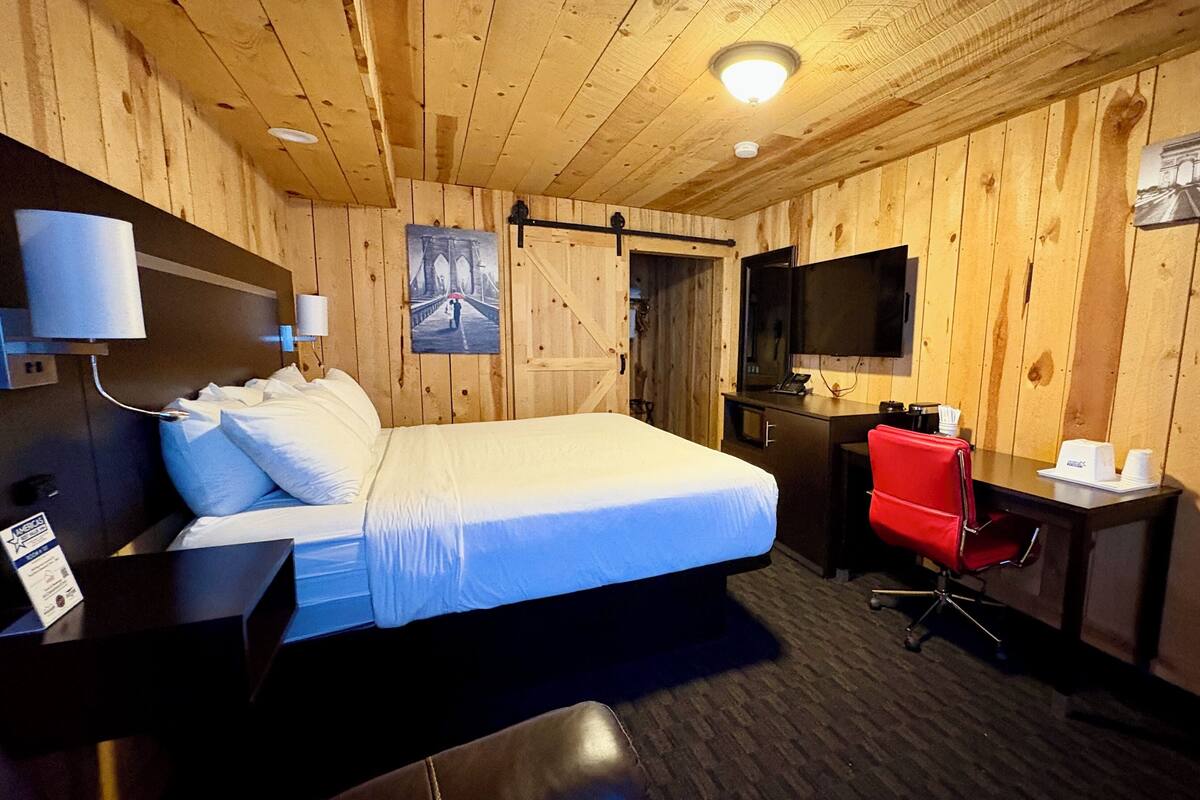 A wooden-paneled room with a bed, desk, chair, and a flat-screen TV.
