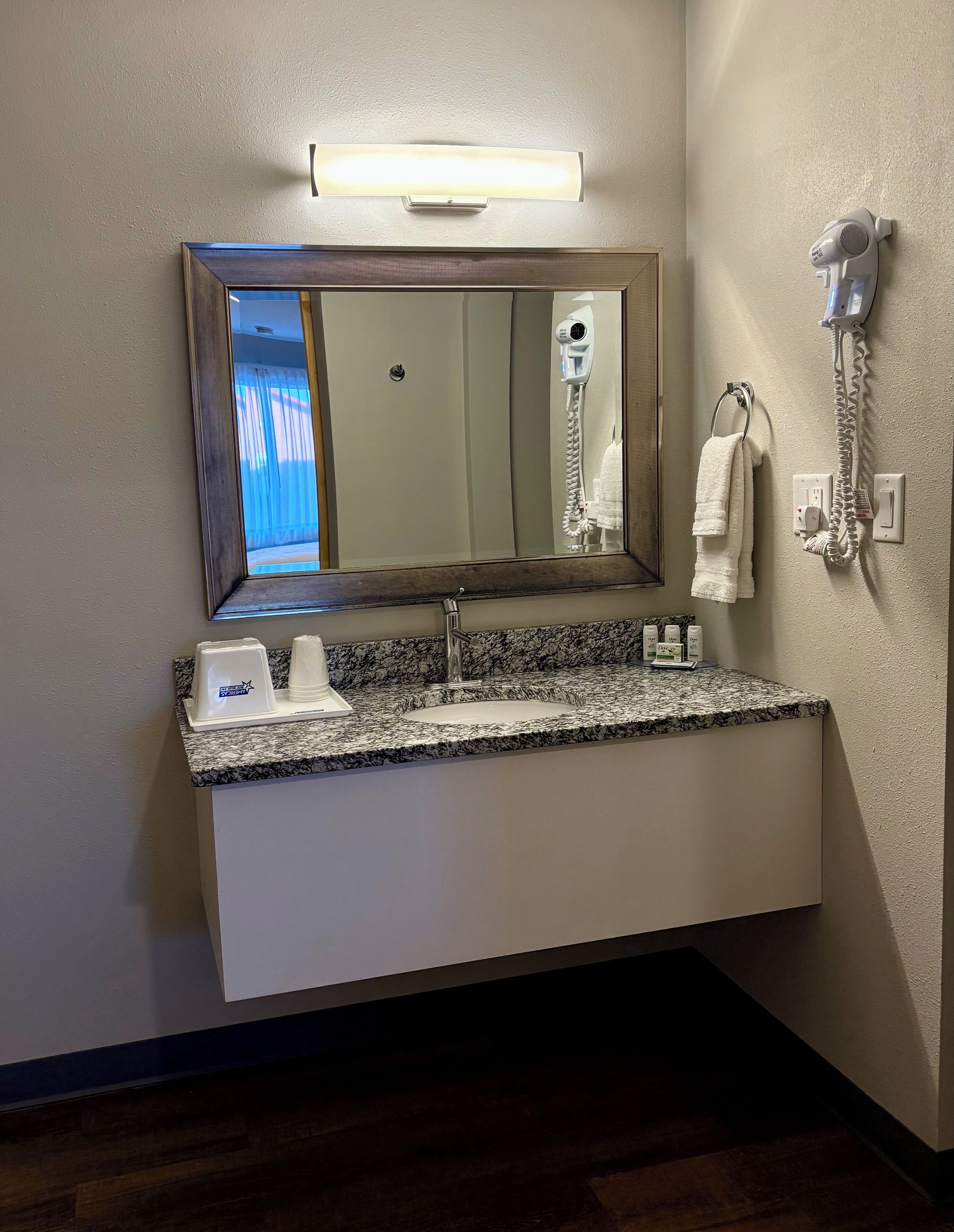 A bathroom with a granite countertop, a sink, a mirror, a hairdryer, and a towel rack.