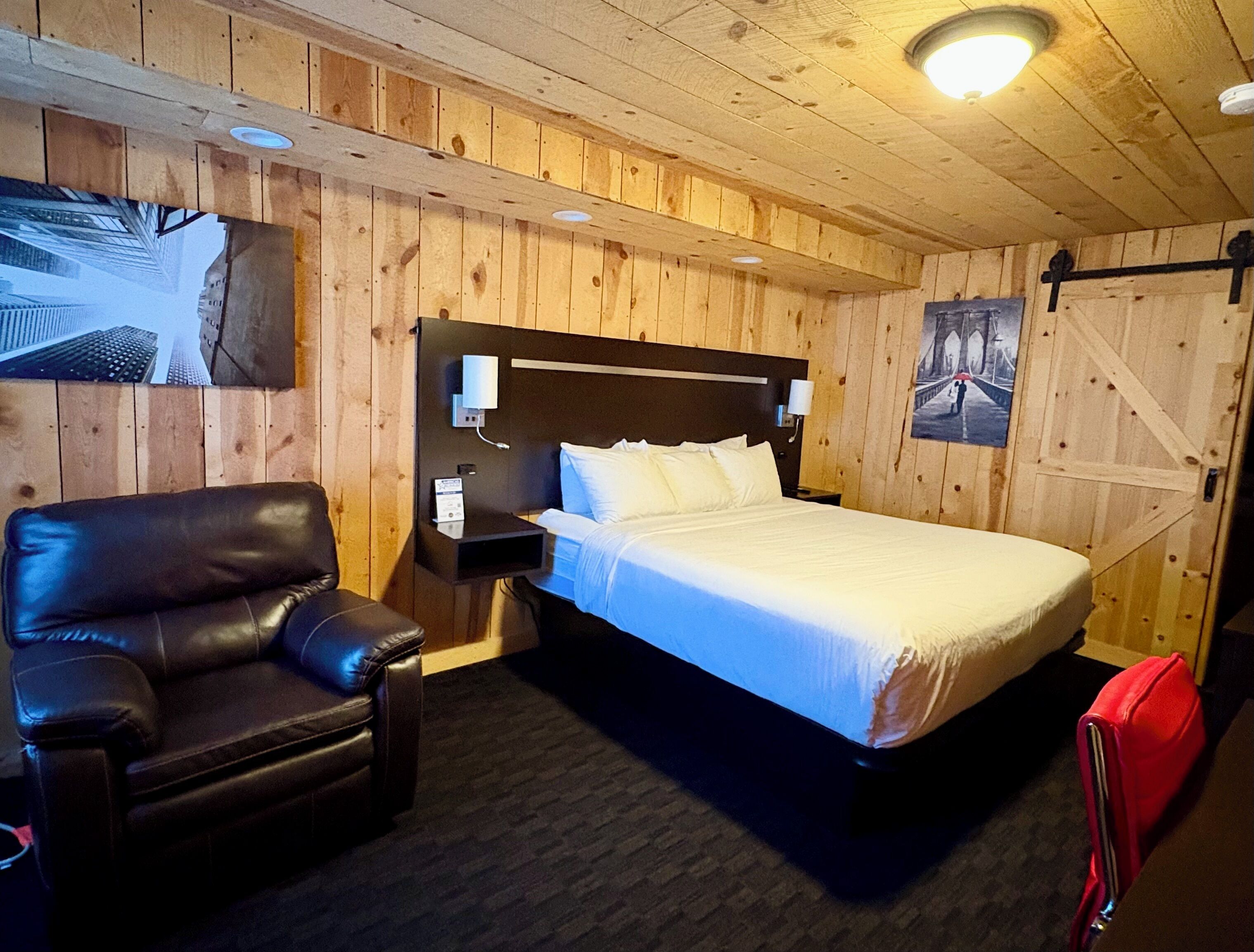 A wooden-paneled room with a bed, a leather chair, and a red bag.