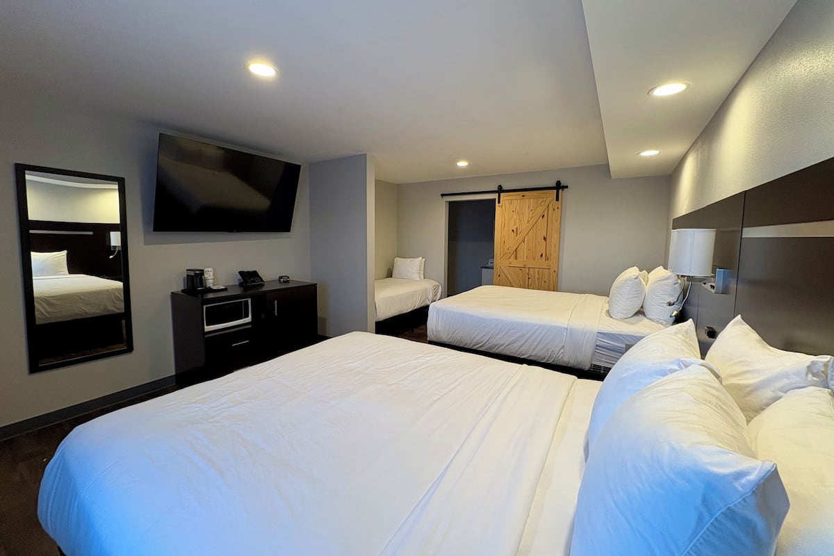 A hotel room with two beds, a TV mounted on the wall, a desk with a phone, and a wooden door.