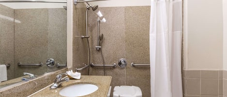 A bathroom with a granite countertop sink, a mirror, a shower with a handheld showerhead, and a white shower curtain.
