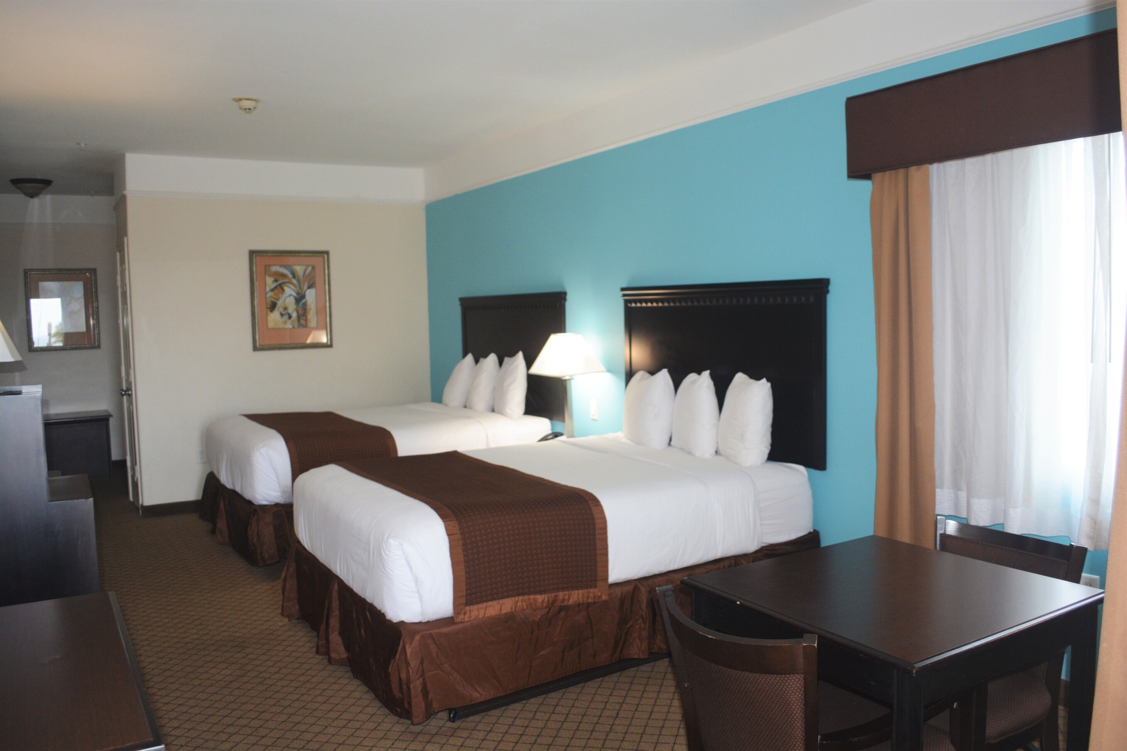 A hotel room with two beds, a desk, and a chair.