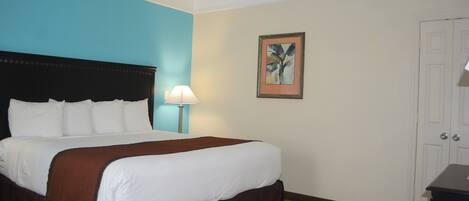 A hotel room with a large bed, a nightstand with a lamp, a framed picture on the wall, and a door.