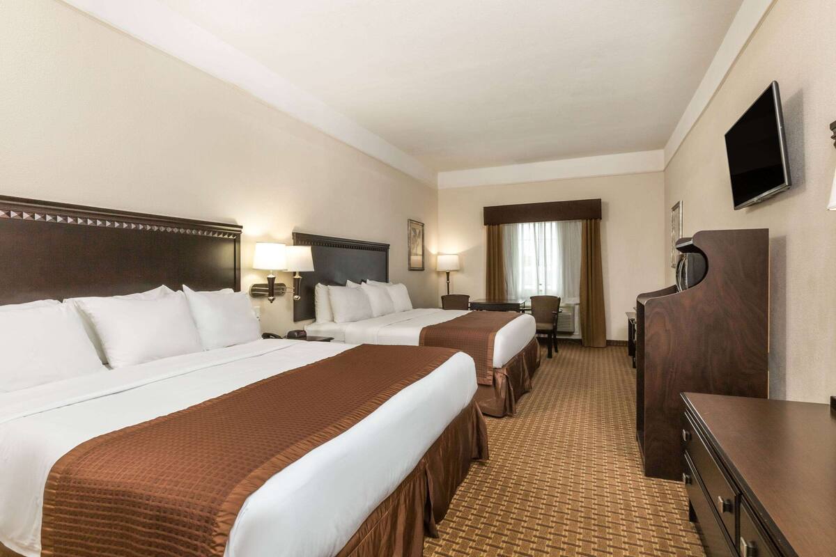 A hotel room with two beds, a desk, a chair, a TV, and a wardrobe.
