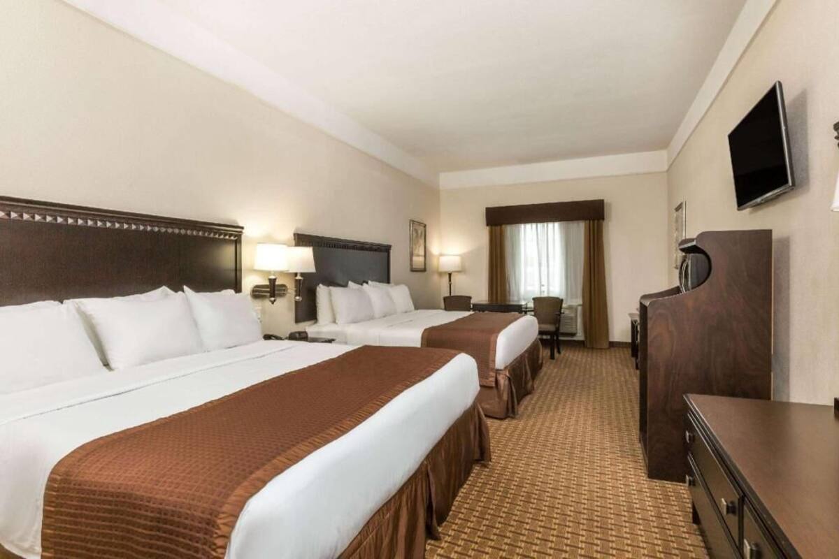 A hotel room with two beds, a desk, a dresser, a TV, and a window with curtains.