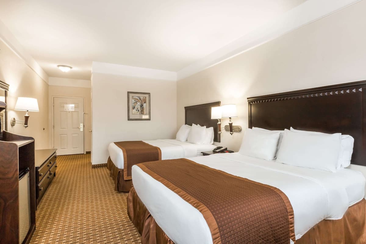 A hotel room with two beds, a dresser, a desk, and a door.