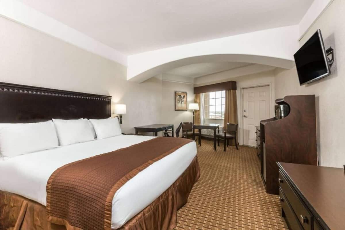 A hotel room with a large bed, a desk, a chair, a television, and a wardrobe.
