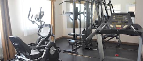 A gym with cardio machines, weightlifting equipment, and a mirrored wall.