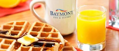 Desayuno con waffles, jarabe, mantequilla, una taza de café y un vaso de zumo de naranja.
