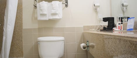 A bathroom with a toilet, a towel rack with folded towels, a hairdryer, and a coffee maker on the counter.
