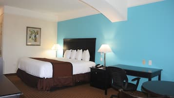 A hotel room with a bed, desk, and chair, featuring a blue accent wall and a patterned carpet.