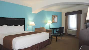 A hotel room with a large bed, a desk, a chair, and a window with curtains.
