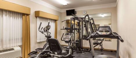 Un gimnasio de hotel con máquinas de cardio, equipo de pesas y un espejo grande.