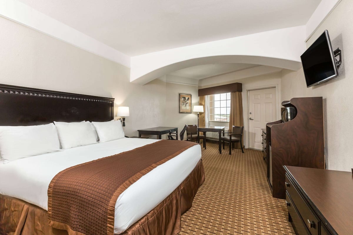 A hotel room with a large bed, a desk, a chair, a television, and a wardrobe.
