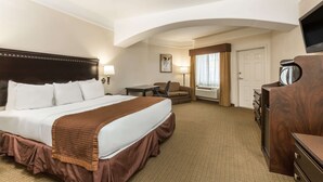 Una habitación de hotel con una cama grande, un escritorio, una silla, un aparador y un televisor.
