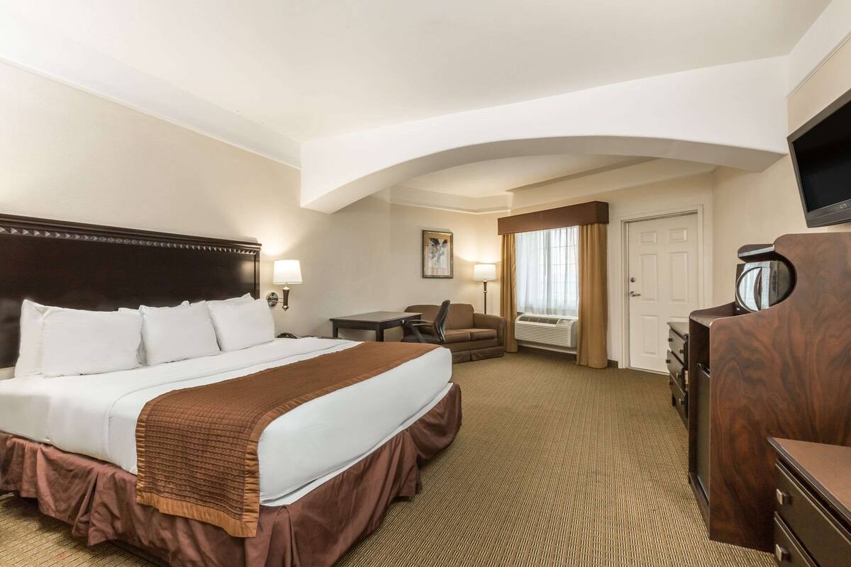A hotel room with a large bed, a desk, a chair, a dresser, and a television.