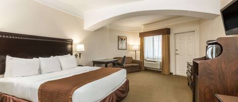 A hotel room with a large bed, a desk, a chair, a dresser, and a television.