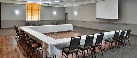 Un salón de conferencias con una larga mesa, sillas, una pantalla de proyector y una araña.