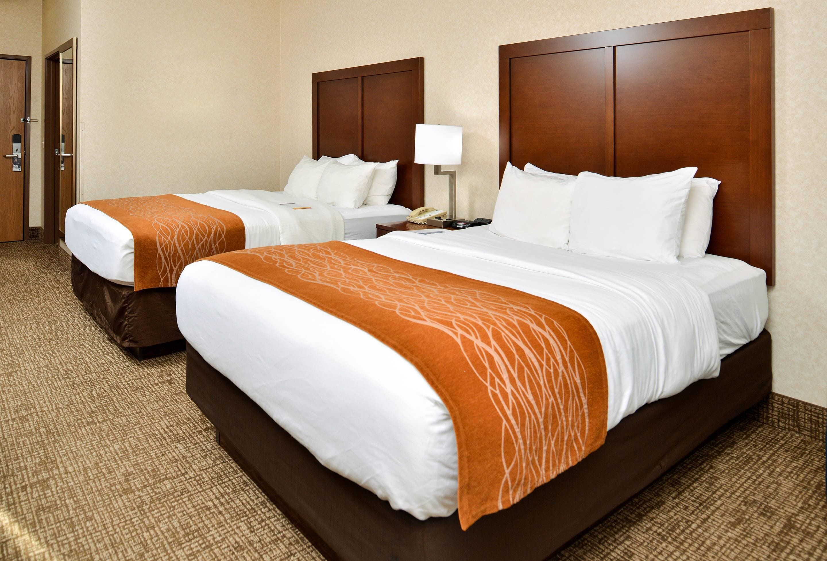 A hotel room with two beds, a nightstand, a lamp, and a door.