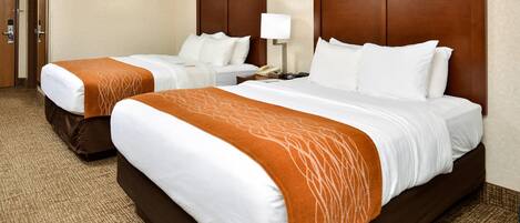 A hotel room with two beds, a nightstand, a lamp, and a door.