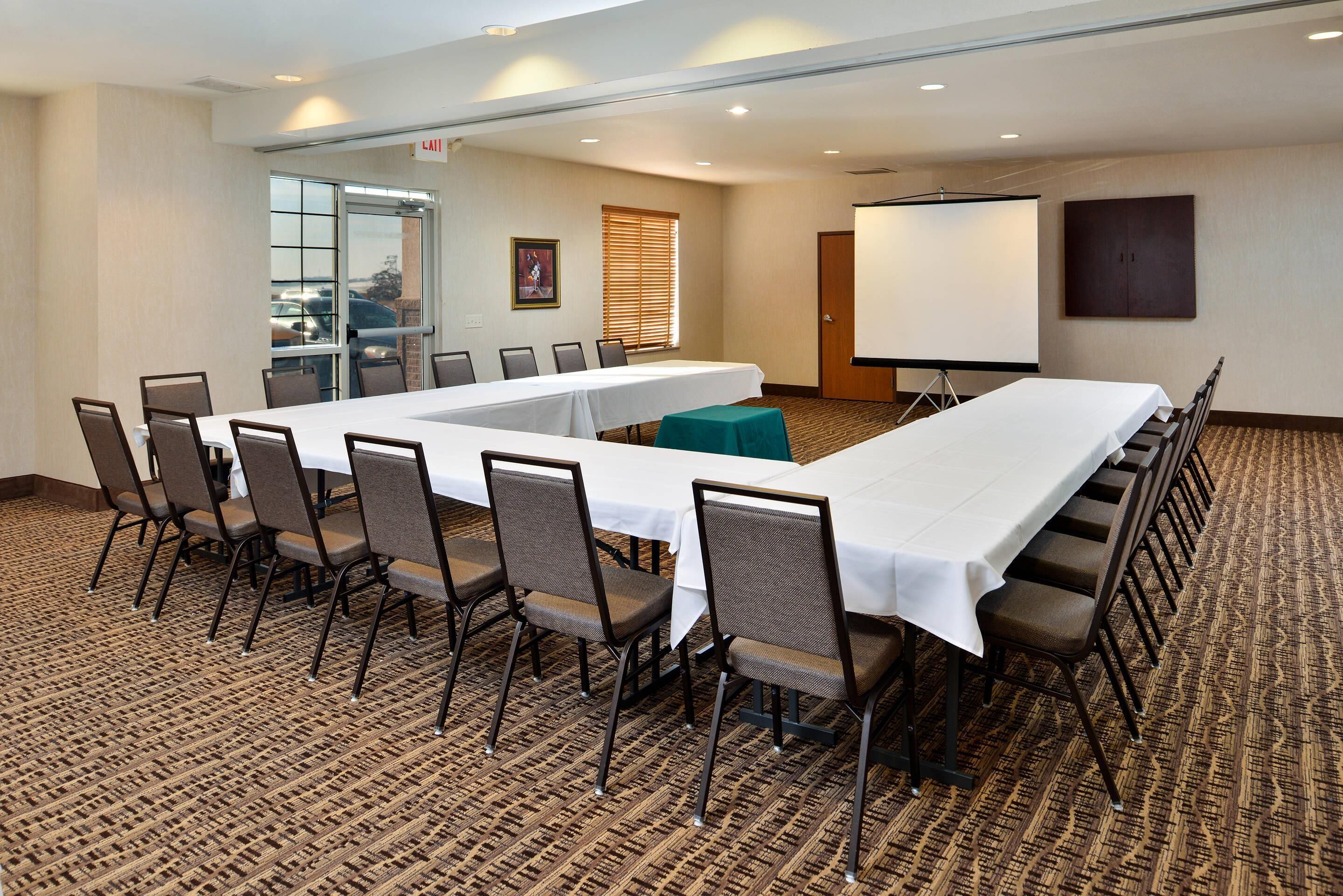 A conference room with a long table, chairs, a projector screen, and a carpeted floor.