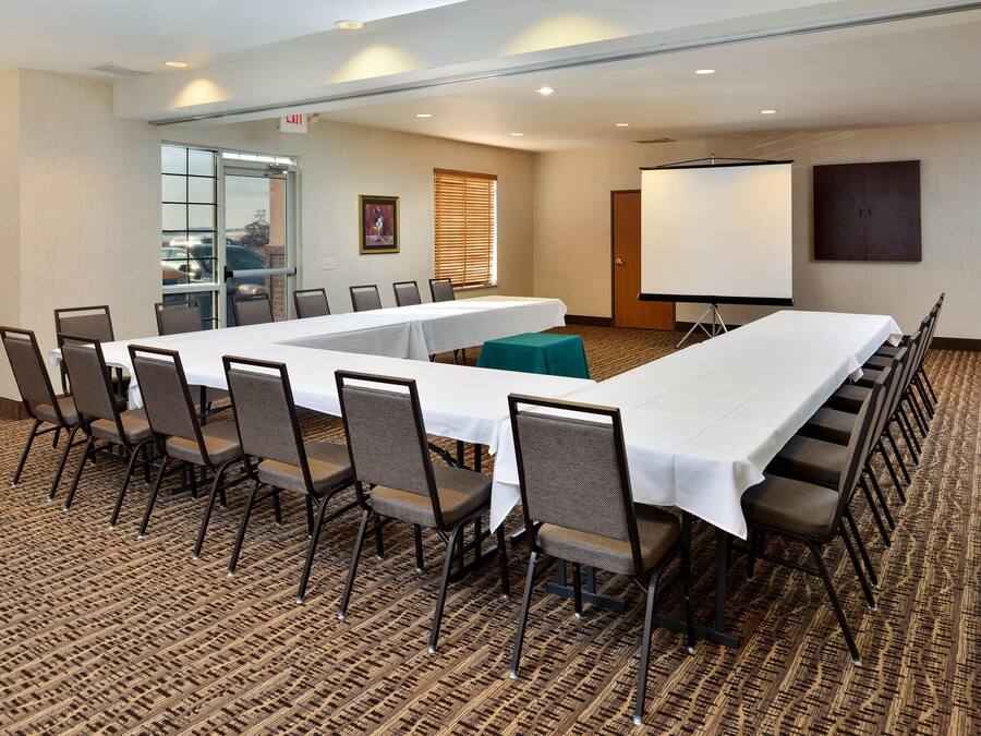 A conference room with a long table, chairs, a projector screen, and a carpeted floor.