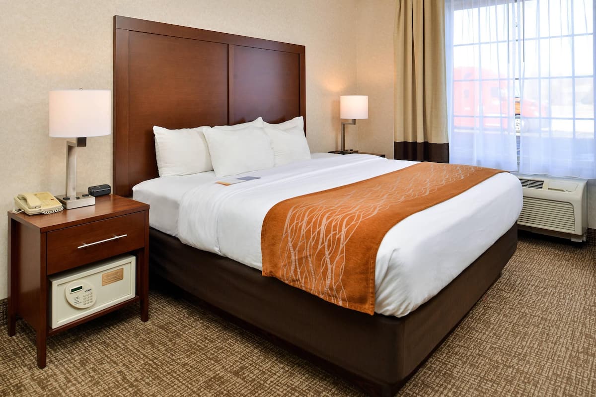 A hotel room with a large bed, bedside lamps, a nightstand with a phone, and a thermostat.