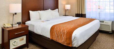 A hotel room with a large bed, bedside lamps, a nightstand with a phone, and a thermostat.