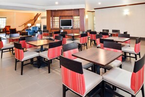 A hotel dining area with multiple tables and chairs, a staircase, and a TV in the background. - Comfort Inn & Suites Madison North (De Forest)