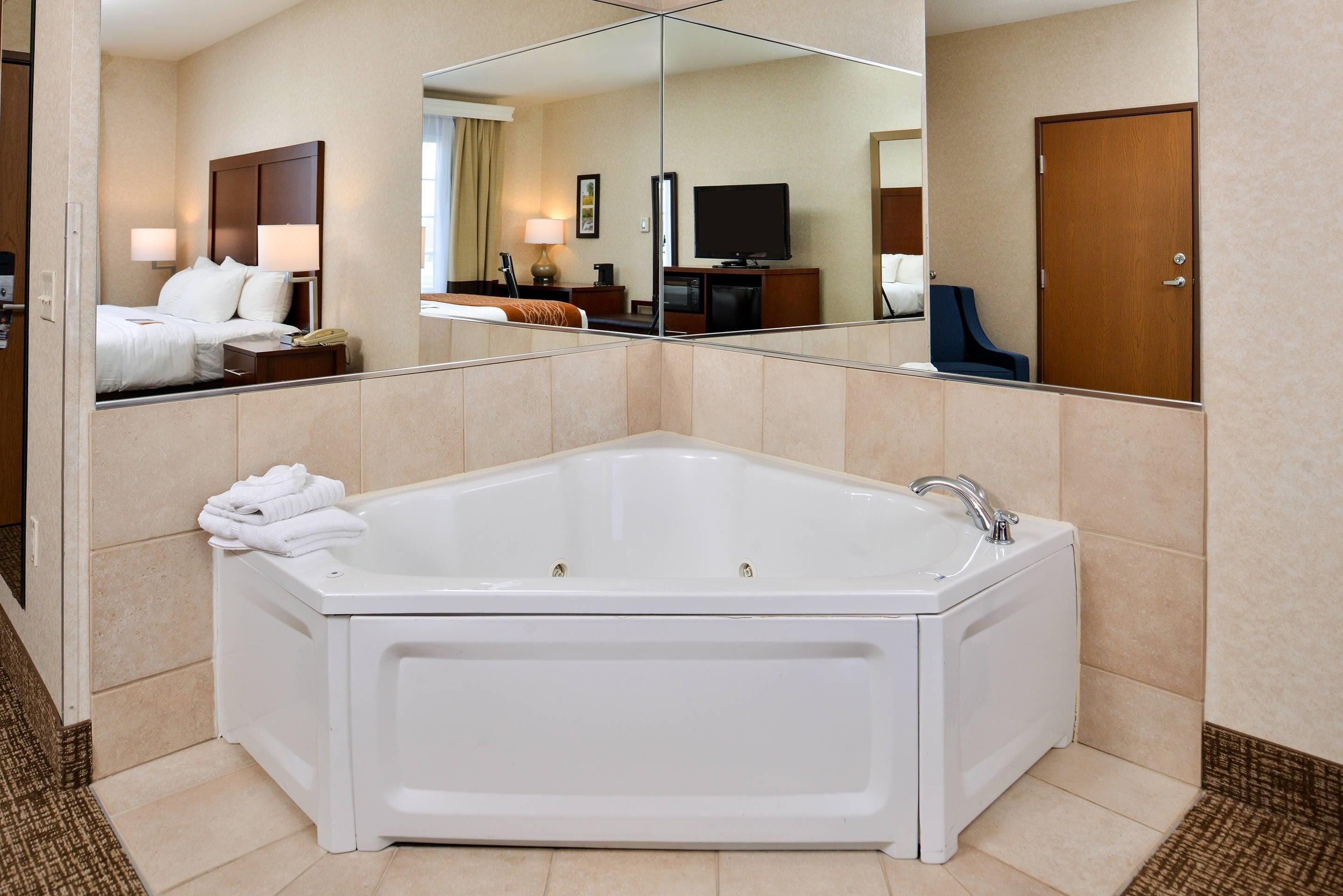A modern hotel bathroom with a large bathtub, a mirror, and a television.