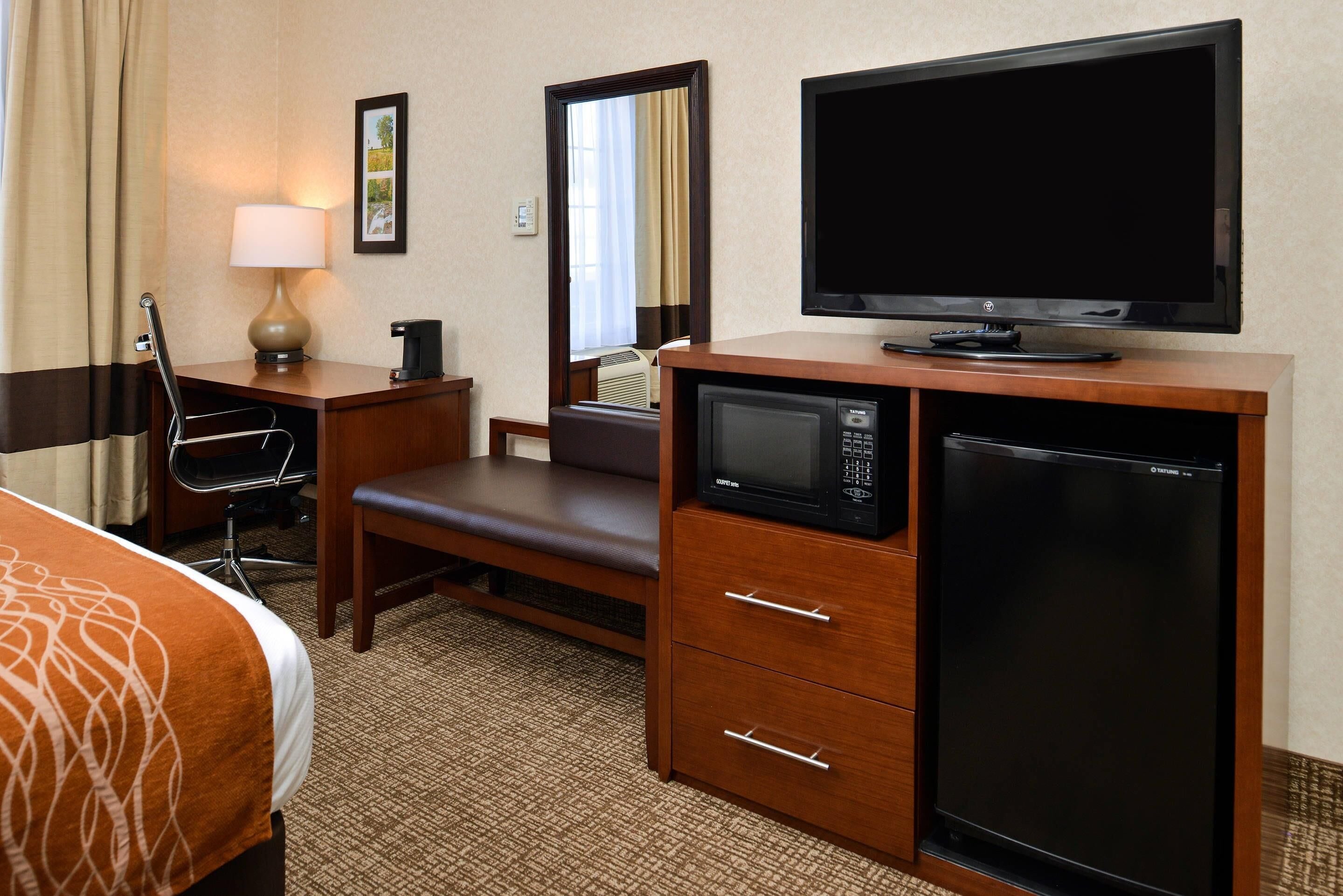 Une chambre d’hôtel équipée d’un lit, d’un bureau, d’une chaise, d’une lampe, d’une télévision, d’un four à micro-ondes, d’un réfrigérateur et d’un miroir.