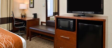 Une chambre d’hôtel équipée d’un lit, d’un bureau, d’une chaise, d’une lampe, d’une télévision, d’un four à micro-ondes, d’un réfrigérateur et d’un miroir.