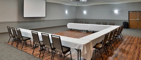 A conference room with a long table, chairs, a projector screen, and a chandelier.