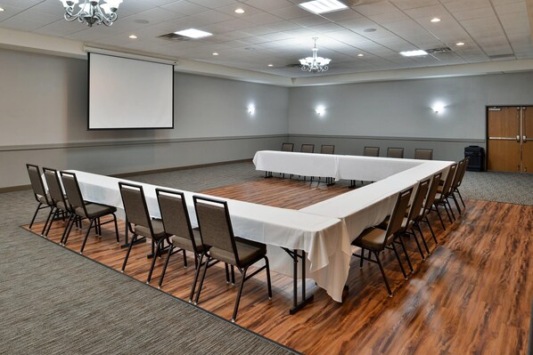 A conference room with a long table, chairs, a projector screen, and a chandelier.