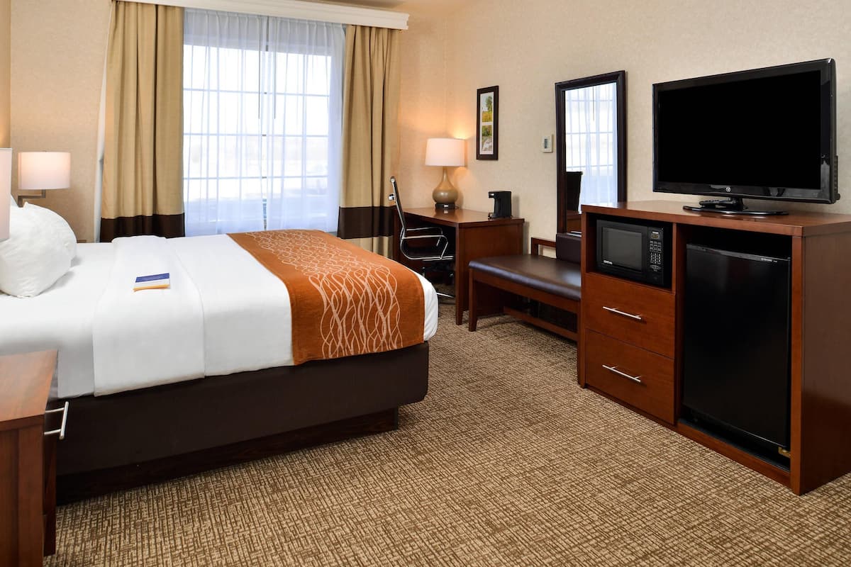 A hotel room with a bed, desk, television, microwave, and a large window with curtains.