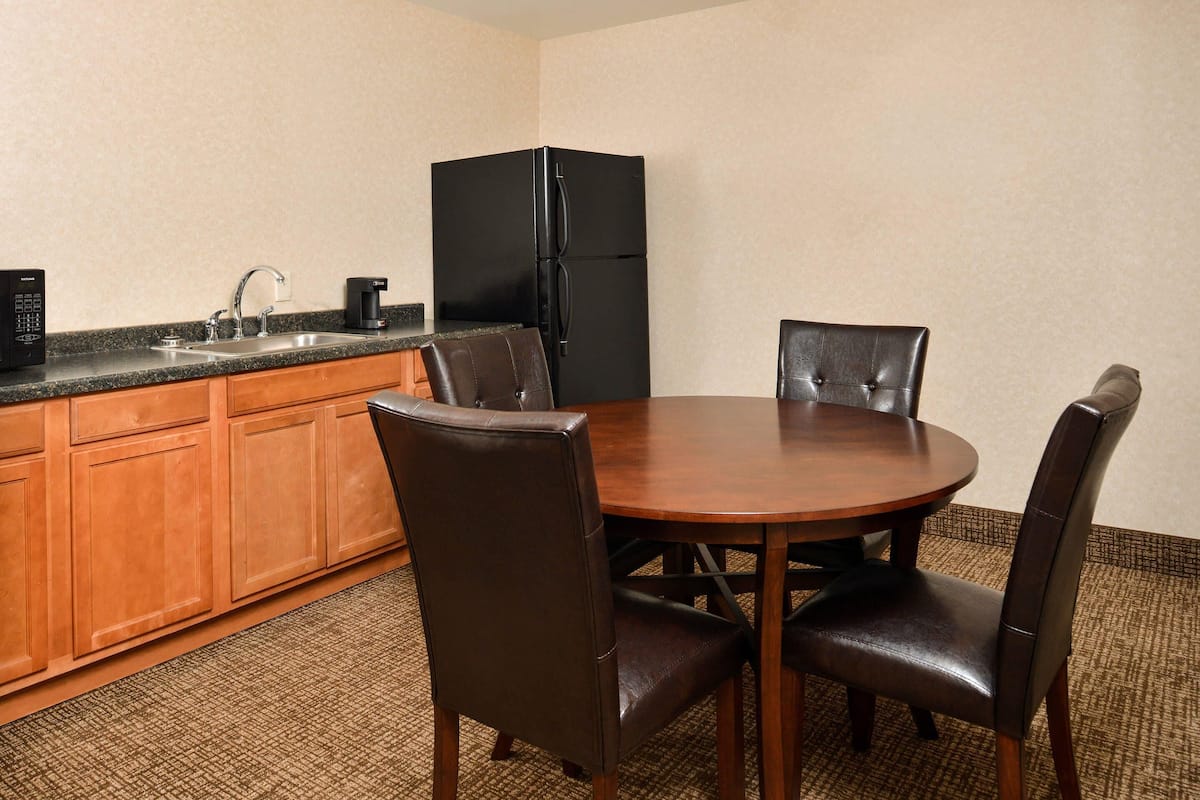 A compact kitchen with a sink, coffee maker, and black refrigerator. There is a round wooden table with four chairs.