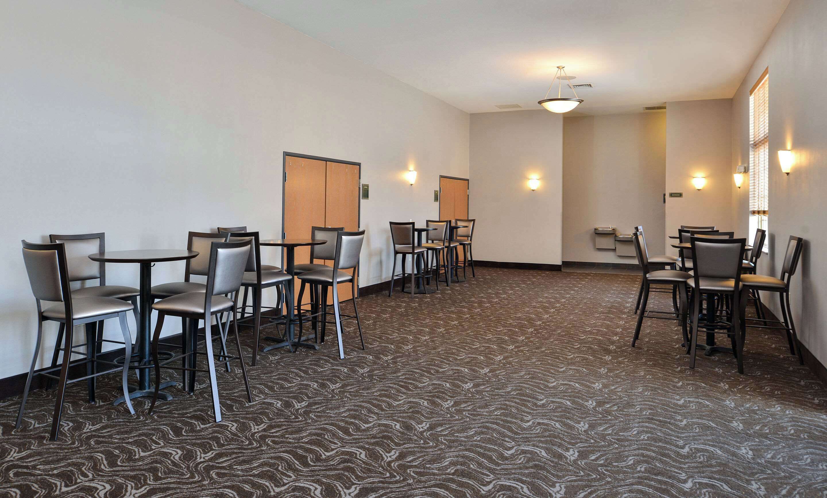 A hotel room with a carpeted floor, multiple tables and chairs, and a door.