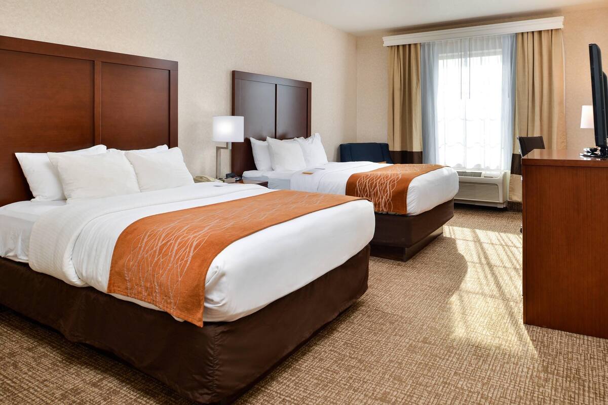 A hotel room with two beds, a desk, a chair, a television, and a window with curtains.