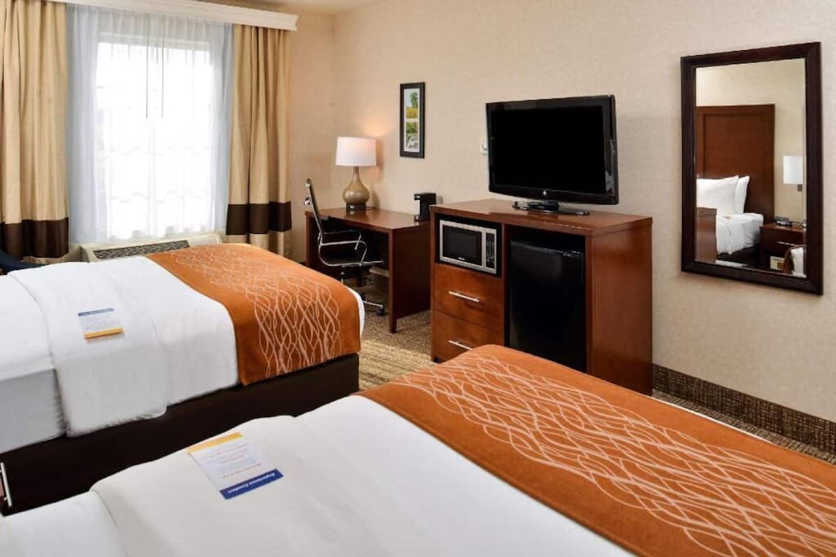 A hotel room with two beds, a desk with a television, a microwave, and a mirror.