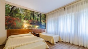 Habitación de hotel con dos camas, un cuadro grande de un paisaje forestal, cabecera de madera y una ventana amplia con cortinas traslúcidas.